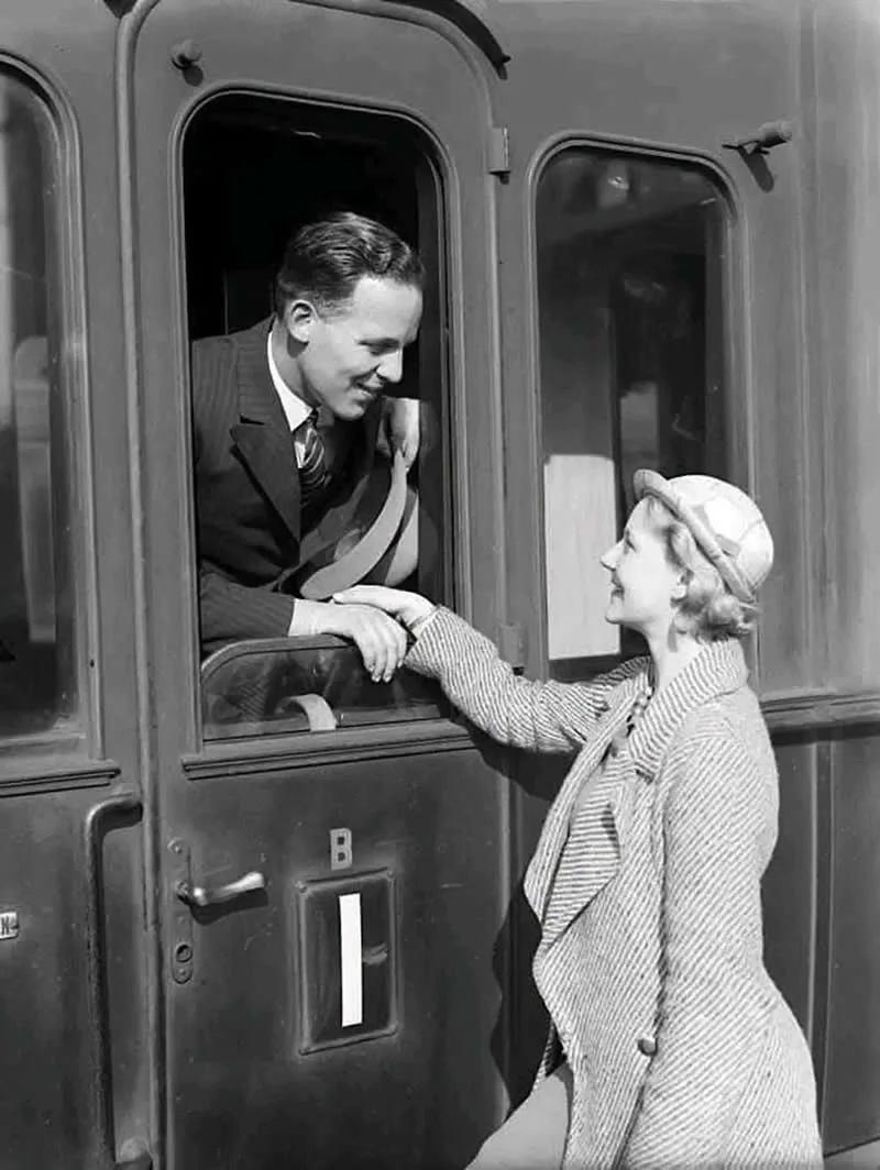 Willem van de Poll: The Master Photographer Who Captured a Changing World 52 Black-and-white photograph of a smiling man in a suit leaning from a train window to hold the hand of a woman wearing a striped coat and hat, capturing a tender farewell on the railway platform.