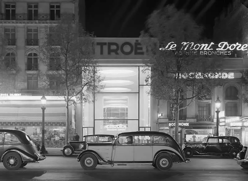 Willem van de Poll: The Master Photographer Who Captured a Changing World 70 Black-and-white photograph of vintage cars parked and driving along a Parisian street at night, with illuminated Citroën and Le Mont Doré storefront signs, historic buildings, and streetlights creating a nostalgic urban scene.